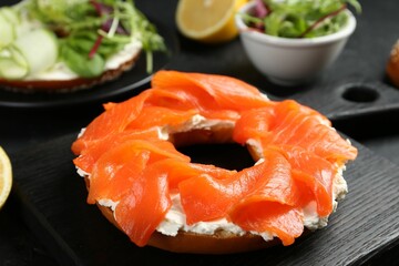 Delicious bagels with salmon and vegetables on black table, selective focus