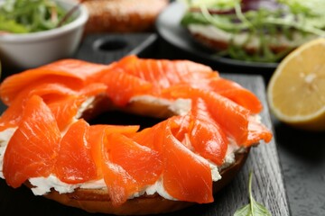 Delicious bagel with salmon and cream cheese n black table, closeup