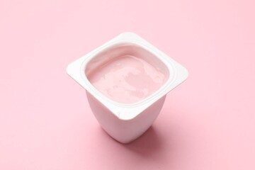 Delicious yogurt in plastic cup on light pink background, closeup