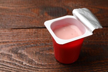 Delicious yogurt in plastic cup on wooden table, closeup. Space for text