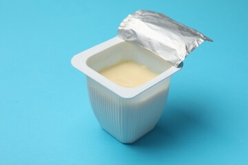 Delicious chocolate yogurt in plastic cup on light blue background, closeup