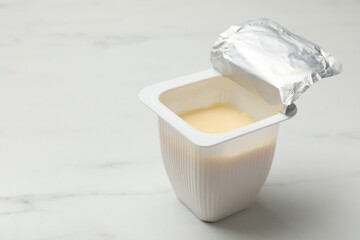 Delicious yogurt in plastic cup on white marble table, closeup. Space for text