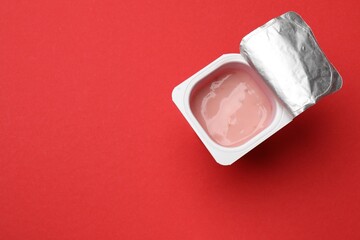 Delicious yogurt in plastic cup on red background, top view. Space for text