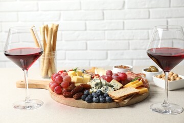 Different types of delicious cheese, other snacks and wine on light grey table