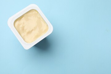 Delicious yogurt in plastic cup on light blue background, top view. Space for text