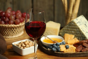 Red wine and different snacks served on wooden table, closeup
