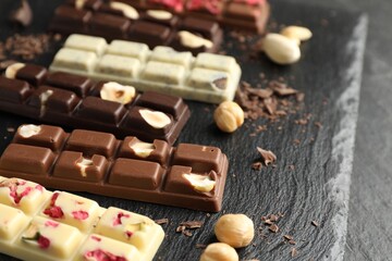Different tasty chocolate bars with nuts and freeze dried raspberry on black table, closeup