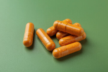 Many turmeric capsules on light green background, closeup