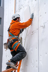 Industrial climber placing a polyfoam sheet insulation to a wall of the building