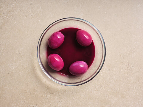 A bowl filled with rich beetroot soup surrounds several pink eggs, highlighting a traditional Ukrainian recipe. This step in the cooking process presents a vibrant and inviting dish