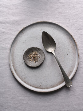 A minimalistic dining setup features a clean, empty plate accompanied by a small bowl of seasoning and a silver spoon, all placed on a neutral linen tablecloth
