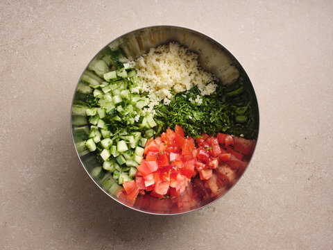 Chopped cucumber, fresh parsley, diced tomatoes, and couscous are neatly arranged in a mixing bowl, showcasing the vibrant colors and textures ideal for making authentic tabbouleh salad.