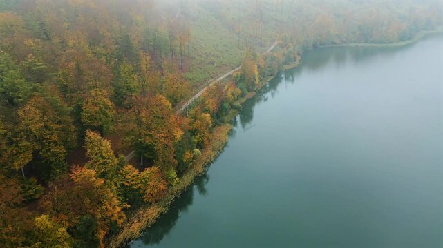 4K drone shot over scenic Kashubia. Forest and Ostrzyckie lake. Moody morning light. Fog in the background.