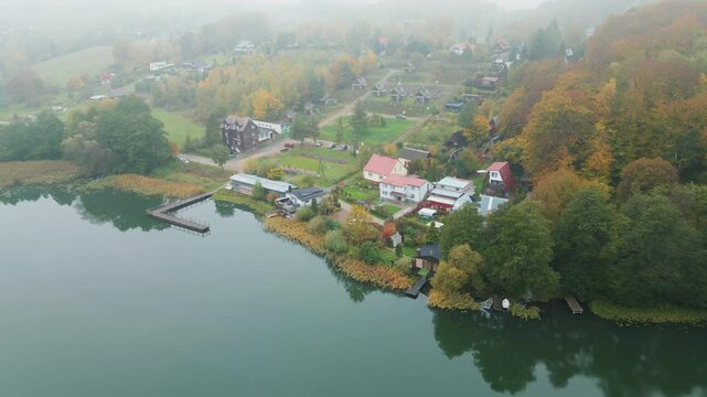 4K drone shot over scenic Kashubia. Forest and Ostrzyckie lake. Krzeszna village. Moody morning light. Fog in the background.
