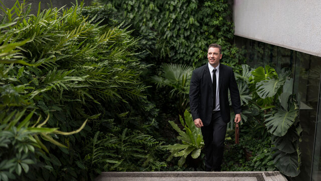 Businessman ceo manager walking up stairs amidst green buildings ESG concept of green business in sustainable development goals Green building Modern building in green city environmental friendly
