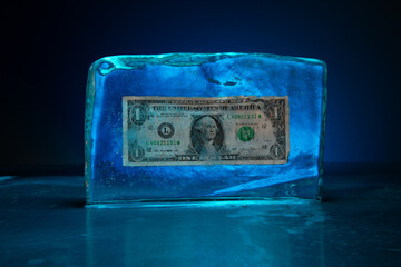 Block of ice encasing a frozen one dollar bill illuminated by blue light