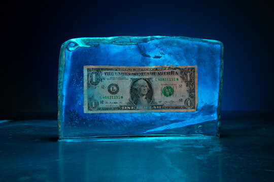 Block of ice encasing a frozen one dollar bill illuminated by blue light