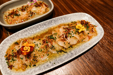 close up of Spanish tapas starter appetizer raw uncooked scallop ceviche with sauce and copy space on a white plate and wooden table