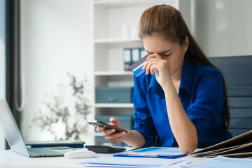 An Asian businesswoman in a blue formal shirt is working at her desk, analyzing financial charts on...