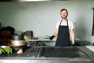 Joyful chef with tongs preparing to grill meat for tacos in a restaurant kitchen