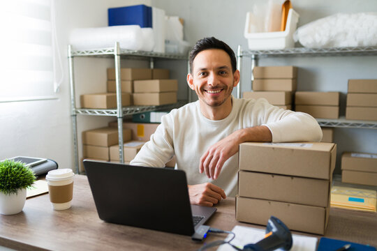 Latino entrepreneur joyfully fulfilling shipping orders from his home office with a laptop and barcode scanner