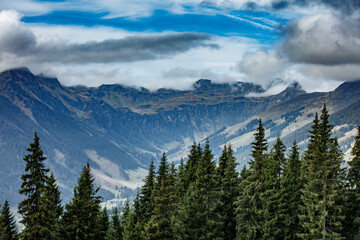 Majestic mountains surround a serene valley in Salzburg, Oostenrijk with wispy clouds and evergreen trees under a cloudy sky
