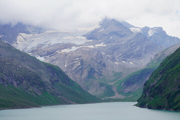 Kaprun high mountain reservoirs, Stausee Mooserboden coastline - cloudy summer day, August 20, 2024. Mountains, glacier, water reservoir under the rainy cloudy sky but nice view before the storm.