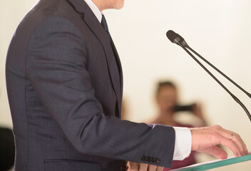 unrecognizable businessman in blue suit speaks into microphones at event