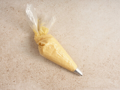 A pastry bag is positioned on a smooth kitchen countertop. It is filled with a yellow batter, shaped for easy handling and precise decorating. This setup suggests preparation for dessert decoration