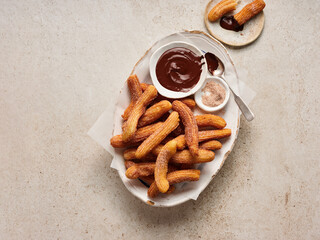 Churros are arranged on a decorative platter, served with rich chocolate sauce and cinnamon sugar. Ideal for dessert lovers enjoying a flavorful afternoon snack