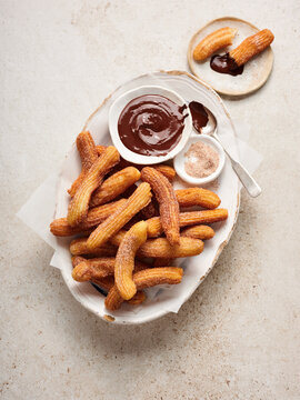 Freshly made churros are arranged on a rustic platter, accompanied by bowls of rich chocolate sauce and sugar, perfect for dipping and enjoying