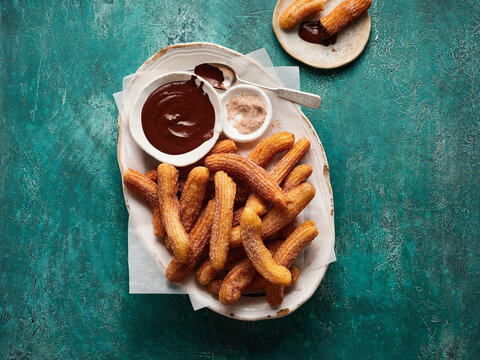 Delicious churros are arranged on a platter, accompanied by a bowl of chocolate sauce and a small dish of cinnamon sugar, creating a tempting dessert display