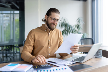 A focused professional reviews paperwork while working on financial or business tasks at a desk...