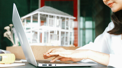 Closeup portrait of skilled architect hand compare between blueprint and house model. Project manager using laptop to analysis architectural construction. Design concept. Focus on hand. Manipulator.