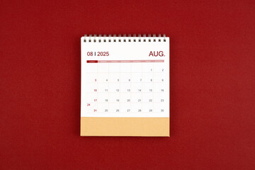 August 2025 desk calendar on red leather.