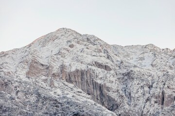 At dawn, the rugged mountain range is blanketed in fresh snow, showcasing its natural beauty. Soft sunlight reflects off the icy surfaces, creating a tranquil atmosphere