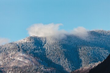 Frosted mountains rise majestically against a clear blue sky, with clouds gently resting on the...