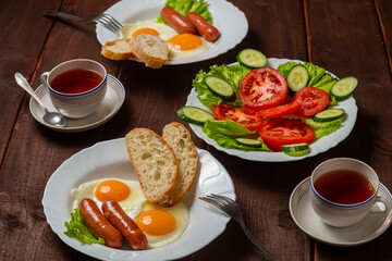 Breakfast for two fried eggs with sausages crispy white bread, salad with tomatoes