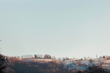 Beneath a vast, clear sky, rolling hills adorned with patches of snow create a peaceful winter panorama. The scene captures the quiet essence of nature in a tranquil afternoon