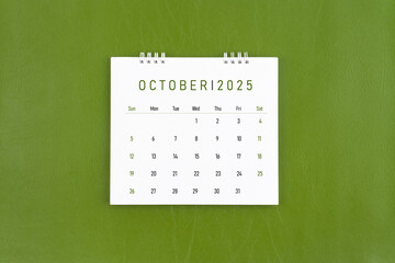 October 2025 Monthly desk calendar on green leather background.