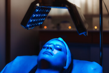 Facial treatment with led therapy. Girl on a light therapy procedure. LED lamp with blue light. Woman in protective glasses