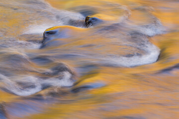 Autumn landscape of the Little River captured with motion blur and illuminated by reflected color from sunlit autumn foliage and blue sky overhead, Great Smoky Mountains National Park, Tennessee, USA