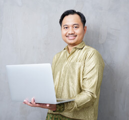Adult Asian man wearing batik smiling at camera while using his laptop - Indonesia men