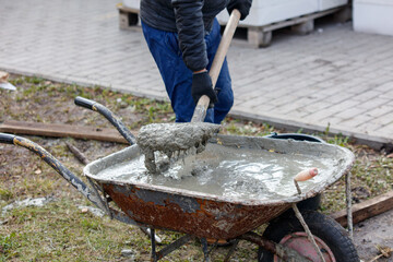 A man is using a shovel to fill a wheelbarrow with concrete