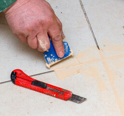 A man is using a blue putty knife to apply a patch to a tile