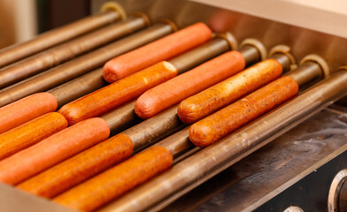 A row of hot dogs are being cooked on a grill