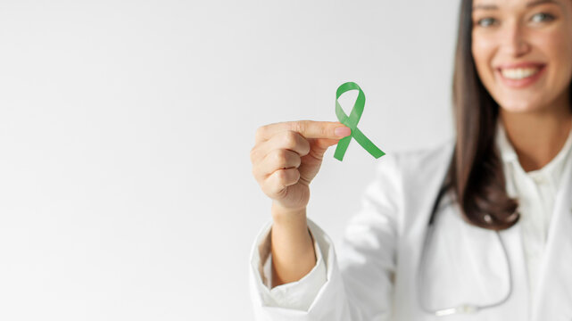 Woman doctor in white uniform holding green ribbon, symbol of world bipolar day, mental health awareness day, Cerebral palsy. World kidney day concept