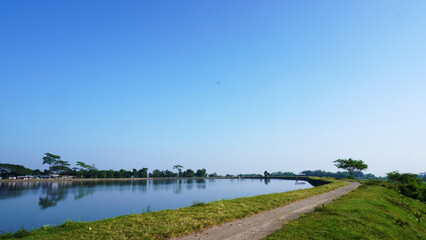 Tranquil Riverside Pathway Along a Reflective Waterbody Under Clear Blue Skies