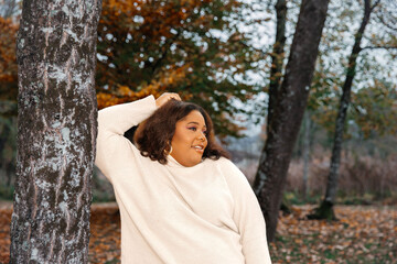 Content hispanic young female in autumn forest wearing cream sweater