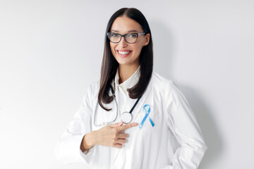 Prostate cancer. Woman doctor pointing at blue ribbon, standing over white background and smiling...